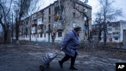 A local woman walks to the distribution point of humanitarian aid in front of housing which was damaged by Russian shelling in Kupiansk, Kharkiv region, Ukraine, Dec. 28, 2022. 