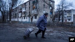 খারখিভ অঞ্চলের কুপিয়ানস্ক-এ রুশ গোলাবর্ষণে ক্ষতিগ্রস্ত আবাসনের সামনে দিয়ে হেঁটে যাচ্ছেন এক স্থানীয় নারী, ২৮ ডিসেম্বর ২০২২।