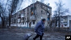 Žena hoda do mjesta za distribuciju humanitarne pomoći ispred stambenog objekta oštećenog ruskim granatiranjem u Kupiansku, oblast Harkov, Ukrajina, 28. decembra 2022. (AP Photo/Evgeniy Maloletka) 