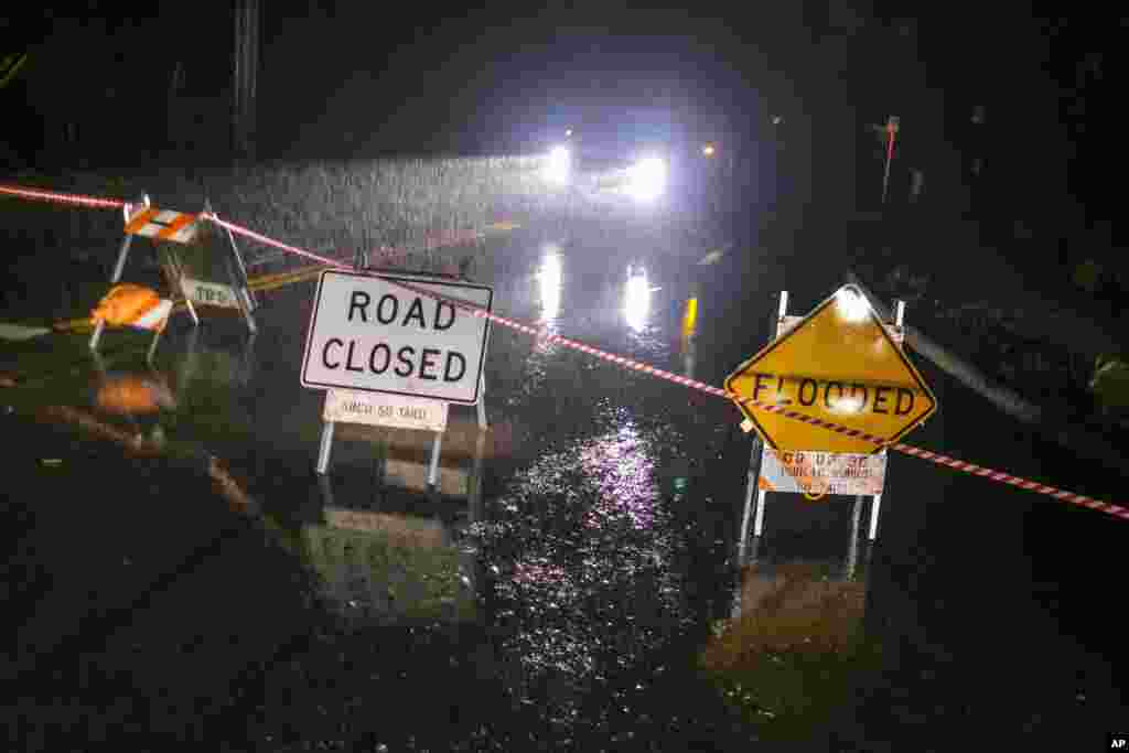 A flooded warning sign and a road closed to thru traffic sign are seen in Montecito, California, Jan. 9, 2023.