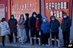 北京市民在宣传习近平思想的标语墙前排队等候接受核酸检测。（2022年12月5日）