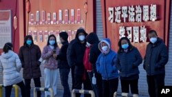 北京市民在宣传习近平思想的标语墙前排队等候接受核酸检测。（2022年12月5日）