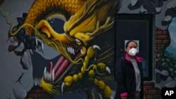 A woman wearing a face mask stands near a mural depicting a dragon in Beijing, Nov. 23, 2022. 