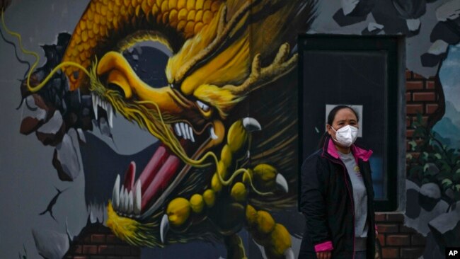 A woman wearing a face mask stands near a mural depicting a dragon in Beijing, Nov. 23, 2022.
