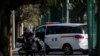 A delivery rider stands near a policeman monitoring inside a police vehicle parked near the site of last weekend's protest in Beijing, China, Nov. 30, 2022. 