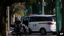 A delivery rider stands near a policeman monitoring inside a police vehicle parked near the site of last weekend's protest in Beijing, China, Nov. 30, 2022. 