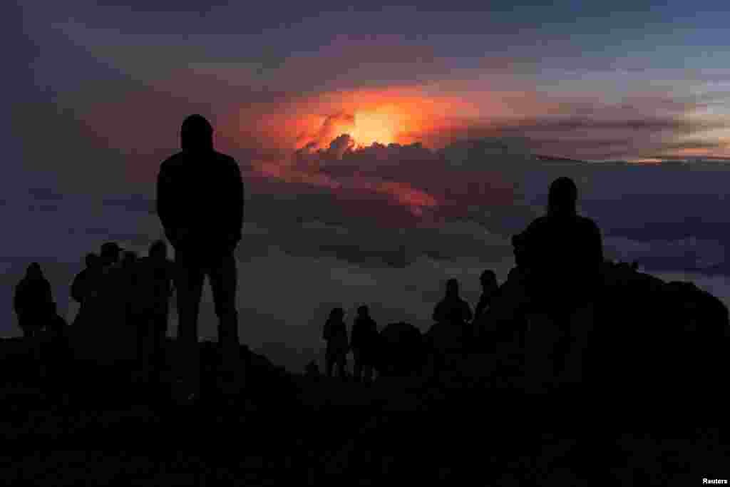 People gather to watch the eruption of the Mauna Loa Volcano while the lava flow is covered with the clouds in Hawaii, Dec. 3, 2022. 
