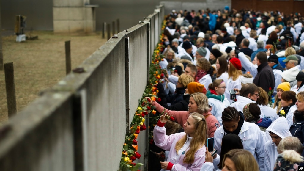 People stick flowers in the remains of the Berlin Wall during a commemoration ceremony to mark the 30th anniversary of the wall's fall at a memorial site at Bernauer Strasse in Berlin, Germany, Nov. 9, 2019. 