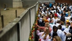 People stick flowers in the remains of the Berlin Wall during a commemoration ceremony to mark the 30th anniversary of the wall's fall at a memorial site at Bernauer Strasse in Berlin, Germany, Nov. 9, 2019. 