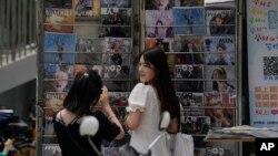 一個姑娘在北京一家書報亭懸掛的時尚雜誌封面前拍照，其中有封面是吳亦凡的照片。（2021年8月1日）