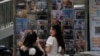 一个姑娘在北京一家书报亭悬挂的时尚杂志封面前拍照，其中有封面是吴亦凡的照片。（2021年8月1日）
