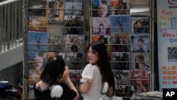 一个姑娘在北京一家书报亭悬挂的时尚杂志封面前拍照，其中有封面是吴亦凡的照片。（2021年8月1日）