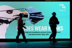 FILE - Essential workers walk past a 'Heroes Wear Masks' sign on the first day of a seven-day lockdown as the state of Victoria looks to curb the spread of a coronavirus disease (COVID-19) outbreak in Melbourne, Australia, May 28, 2021.