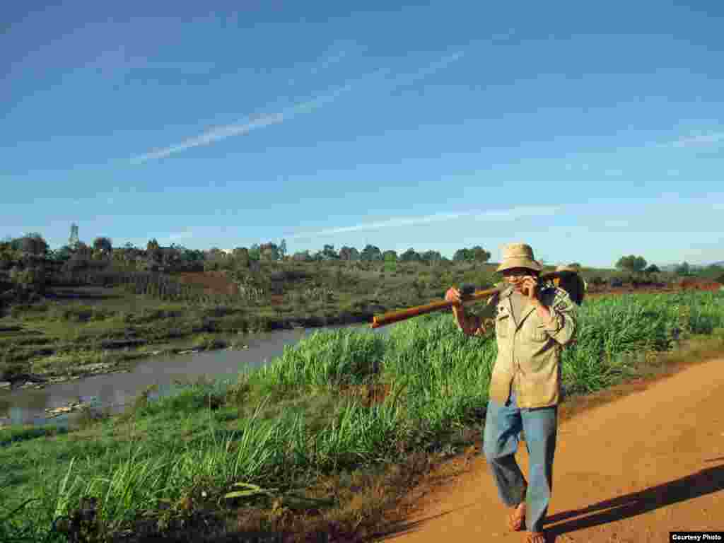 A young Vietnamese man walks in the countryside, carrying gardening tools on his shoulder while talking on his cellphone in Dalat province, South Vietnam. (Photo by Hang Dinh Thi Thanh/Vietnam/VOA reader)