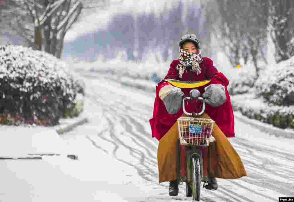 A woman rides her electric bicycle along a street during snowfall in Lianyungang, Jiangsu province, China.