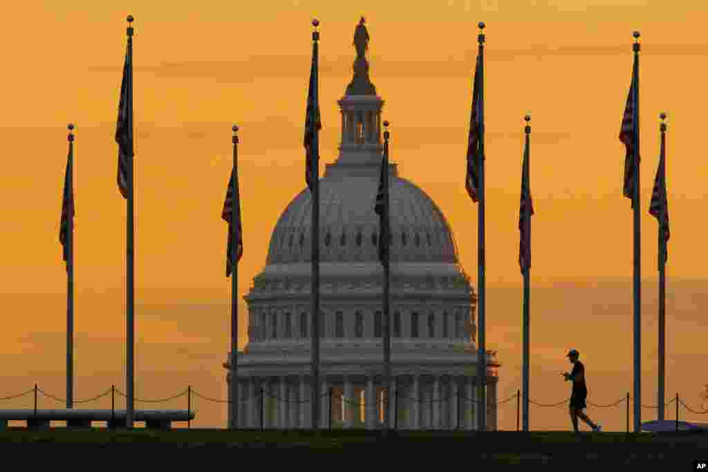 A person is in front of the sunrise as he walks through the U.S. Flags on the National Mall in Washington, D.C.