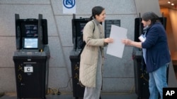 A voter smiles as she hands a privacy sleeve to a poll worker after casting her ballot in an electronic counting machine at a polling site in the Brooklyn Museum, Nov. 8, 2022, in the Brooklyn borough of New York.