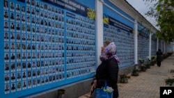 A woman stands in front of the "Memory wall of fallen defenders of Ukraine in Russia-Ukranian war" in downtown Kyiv, Ukraine, Nov. 7, 2022.
