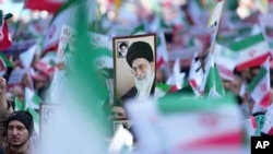 A man holds up a poster of Iranian Supreme Leader Ayatollah Ali Khamenei as others wave the country's flags during a rally in front of the former U.S. Embassy in Tehran, Iran, Nov. 4, 2022.