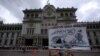 Un manifestante sostiene un cartel con una caricatura que reza "la corrupción genera migración" en una protesta contra el presidente de Guatemala, Alejandro Giammattei, frente al Palacio Nacional de la Cultura en la Ciudad de Guatemala, el 5 de junio de 2021. 