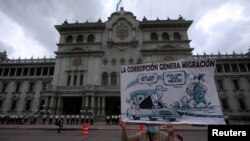 Un manifestante sostiene un cartel con una caricatura que reza "la corrupción genera migración" en una protesta contra el presidente de Guatemala, Alejandro Giammattei, frente al Palacio Nacional de la Cultura en la Ciudad de Guatemala, el 5 de junio de 2021. 