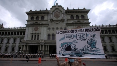 Un manifestante sostiene un cartel con una caricatura que reza "la corrupción genera migración" en una protesta contra el presidente de Guatemala, Alejandro Giammattei, frente al Palacio Nacional de la Cultura en la Ciudad de Guatemala, el 5 de junio de 2021. 