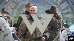 FILE: Visitors wearing military camouflage stand at the entrance of the 'PMC Wagner Centre', which is associated with businessman and founder of the Wagner private military group Yevgeny Prigozhin, in St. Petersburg, Russia. Taken Friday, Nov. 4, 2022