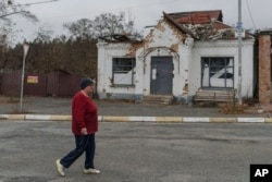 A woman passes an apartment building destroyed by fighting, in the village of Moshun, outside Kyiv, Ukraine, Friday, Nov. 4, 2022.