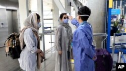 A health worker, right, checks temperature of passengers to help prevent the spread of the coronavirus upon arrival at the departure terminal of Tehran's Imam Khomeini airport, Iran, Friday, July 17, 2020. The first Emirates flight arrived in Iran…