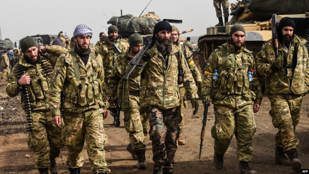 Syrian opposition fighters backed by Turkey walk in front of Turkish troops near the Syria border at Hassa, Hatay province on Jan. 22, 2018. 