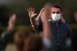 FILE - Brazil's President Jair Bolsonaro, who is infected with COVID-19, wears a protective face mask as he waves to supporters outside his official residence the Alvorada Palace, in Brasilia, Brazil, July 20, 2020.