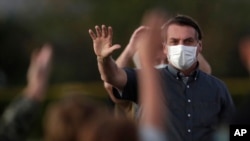 FILE - Brazil's President Jair Bolsonaro, who is infected with COVID-19, wears a protective face mask as he waves to supporters outside his official residence the Alvorada Palace, in Brasilia, Brazil, July 20, 2020.