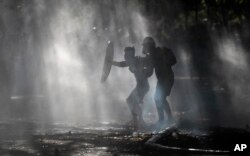 Anti-government demonstrators shield themselves amid the spray of a police water cannon trying to disperse them in Santiago, Chile, Friday, Dec. 27, 2019.
