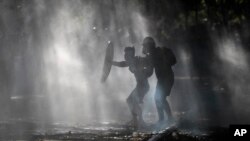 Anti-government demonstrators shield themselves amid the spray of a police water cannon trying to disperse them in Santiago, Chile, Dec. 27, 2019.