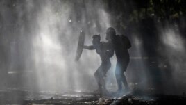 Anti-government demonstrators shield themselves amid the spray of a police water cannon trying to disperse them in Santiago, Chile, Friday, Dec. 27, 2019.