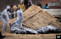 Men wearing protective gear exhume the bodies of civilians killed during the Russian occupation in Bucha, on the outskirts of Kyiv, Ukraine, April 13, 2022.