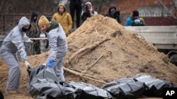 Des hommes portant des équipements de protection exhument les corps de civils tués pendant l'occupation russe à Bucha, à la périphérie de Kiev, Ukraine, le 13 avril 2022 (AP). 