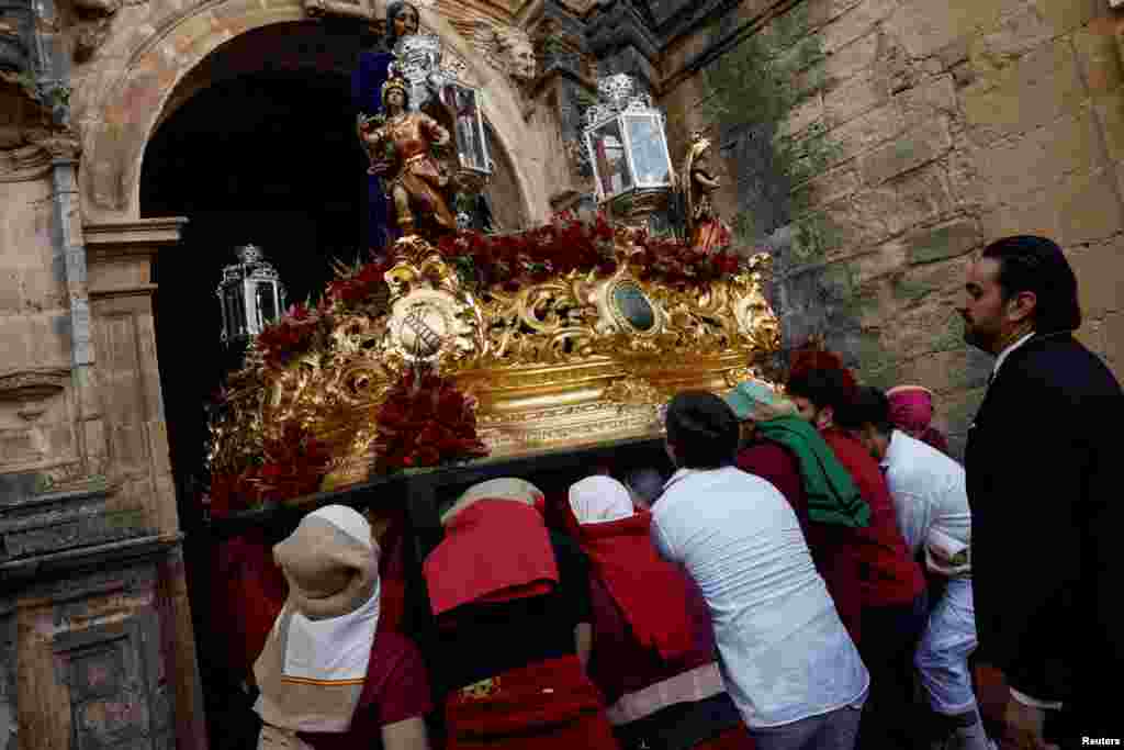 Costaleros pertenecientes a la hermandad de Los Gitanos salen de una iglesia mientras llevan una estatua de Cristo en una estructura conocida tradicionalmente como &#39;paso&#39;.