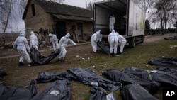 Volunteers load bodies of civilians killed in Bucha onto a truck to be taken to a morgue for investigation, in the outskirts of Kyiv, Ukraine, Tuesday, April 12, 2022.