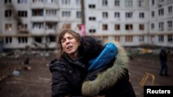 A woman reacts as she hugs another woman outside a heavily damaged apartment block in Kharkiv following an artillery attack amid Russia's invasion of Ukraine, April 13, 2022.