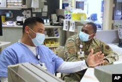 In this image provided by the U.S. Army, U.S. Air Force Tech Sgt. Deundre Bryant, right, a medical administrator, checks up on Tech Sgt. Rony Castaneda-Zamora a medical technician, while supporting the COVID response operations at University of Rochester onFeb.16, 2022. (Spc. Khalan Moore/U.S. Army via AP)