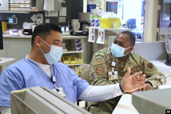 In this image provided by the U.S. Army, U.S. Air Force Tech Sgt. Deundre Bryant, right, a medical administrator, checks up on Tech Sgt. Rony Castaneda-Zamora a medical technician, while supporting the COVID response operations at University of Rochester onFeb.16, 2022. (Spc. Khalan Moore/U.S. Army via AP)