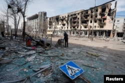 A resident stands with her belongings on a street near a building burnt in the course of the Ukraine-Russia conflict, in the southern port city of Mariupol, Ukraine April 10, 2022. (REUTERS/Alexander Ermochenko)