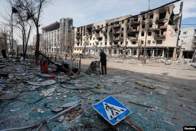 A resident stands with her belongings on a street near a building burnt in the course of the Ukraine-Russia conflict, in the southern port city of Mariupol, Ukraine April 10, 2022. (REUTERS/Alexander Ermochenko)