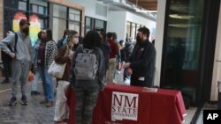 FILE - Students, including Cruz Davis-Martinez, left, in the gray hoody, wait to speak with New Mexico State University recruiter Joshua Rysnek, at their high school, in Santa Fe, N.M., March 10, 2022.