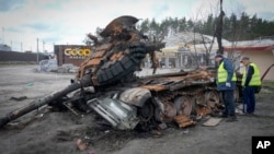Road workers examine a destroyed Russian tank on the highway to Kyiv, Ukraine, April 11, 2022.