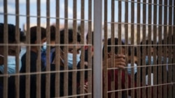 Migrants who crossed the Mediterranean Sea by boat line up behind a fence in Lampedusa, Italy, Oct. 1, 2021, as they wait to board a ferry to Sicily.