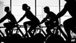 FILE - People are seen exercising on stationary bicycles.