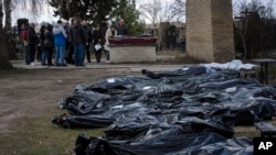 FILE - A family mourns a relative killed during the war with Russia, as dozens of black bags containing more bodies of victims are seen strewn across the graveyard in the cemetery in Bucha, in the outskirts of Kyiv, Ukraine, April 11, 2022.