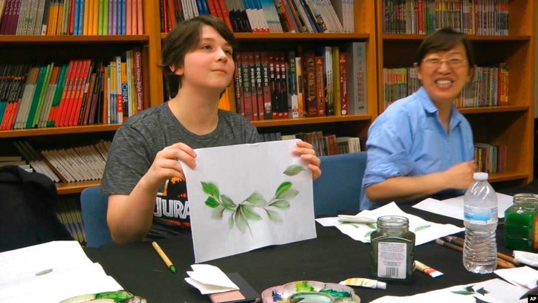 FILE - Undergraduate student Moe Lewis, left, shows her watercolor painting of peony leaves at a traditional Chinese painting class at the Confucius Institute at George Mason University in Fairfax, Va., May 2, 2018.